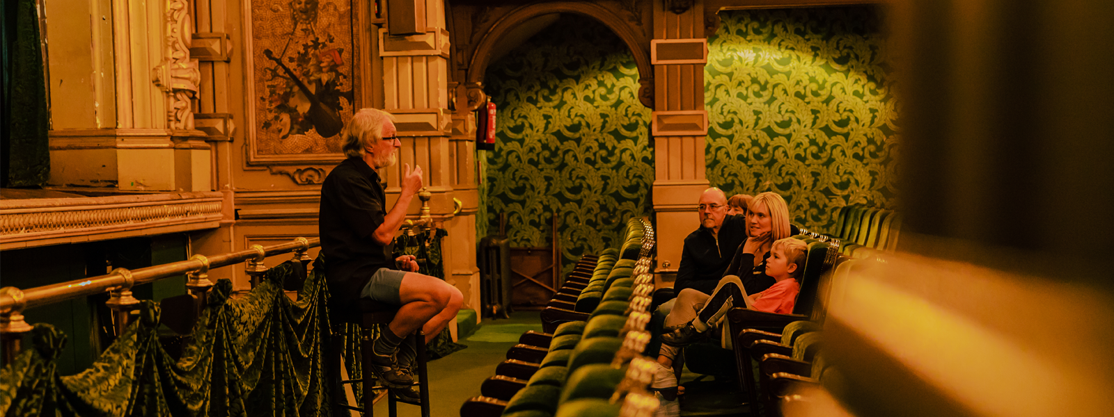 A family enjoying a tour of the Gaiety Theatre on the Isle of Man, the tour guide is showing them pictures of the Theatre's history